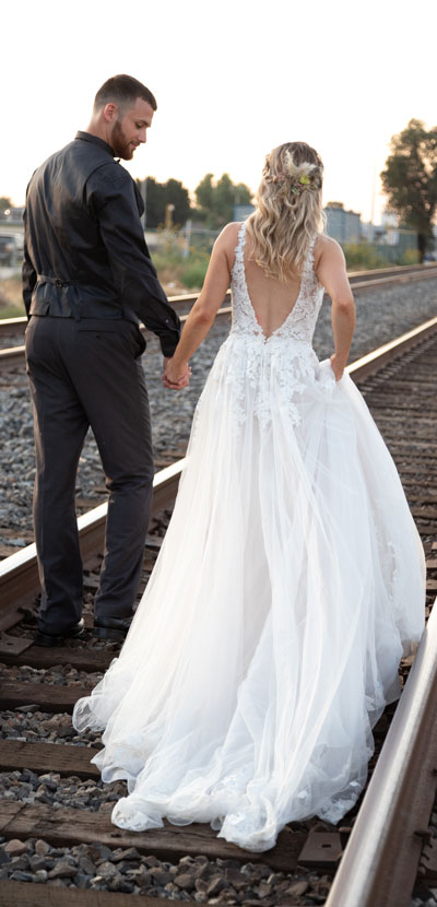 Bride and groom holding hands walking on train tracks