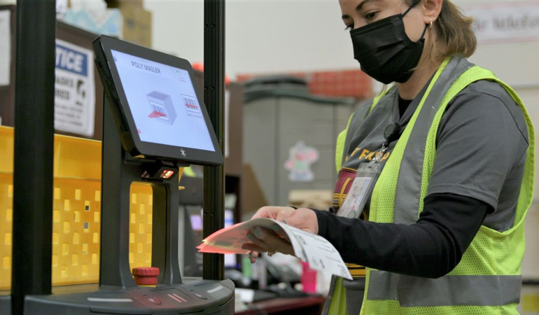 A warehouse worker for Superior Uniform Group scans a shipment label on a collaborative mobile robot from 6 River Systems at a facility in Coppell, Texas.